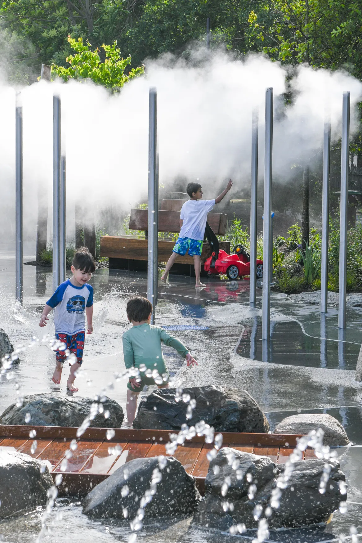 Children playing in a splash park at the Pattern District in Newton Upper Falls, MA, featuring interactive water features and landscaped outdoor space.