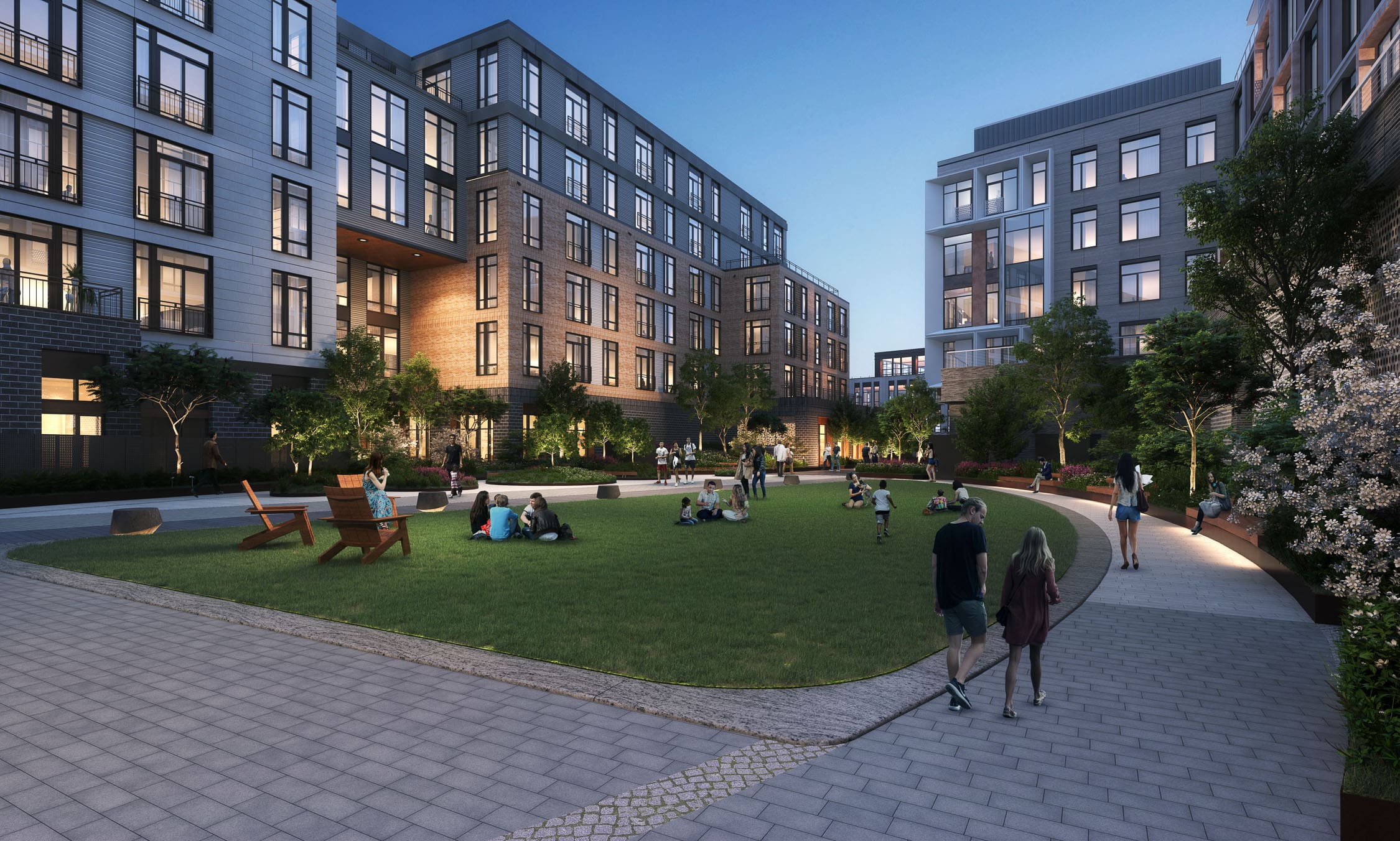 Evening view of a residential courtyard at the Pattern District in Newton Upper Falls, MA, featuring landscaped green space, walking paths, and modern apartment buildings.